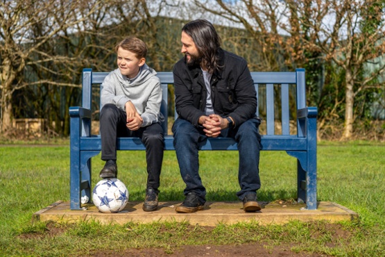 A man and a boy sitting on a bench with a football